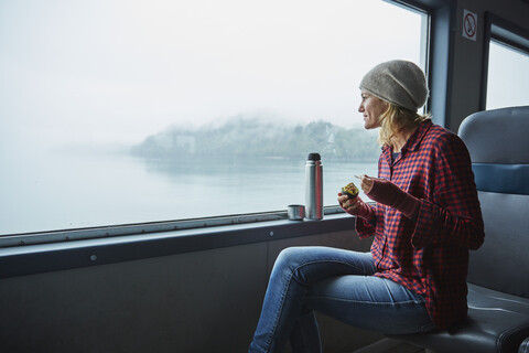 Chile, Hornopiren, Frau schaut aus dem Fenster einer Fähre und isst eine Avocado, lizenzfreies Stockfoto