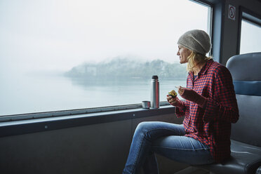 Chile, Hornopiren, Frau schaut aus dem Fenster einer Fähre und isst eine Avocado - SSCF00189