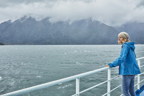 Chile, Hornopiren, Frau steht an der Reling einer Fähre und schaut auf den Fjord, lizenzfreies Stockfoto
