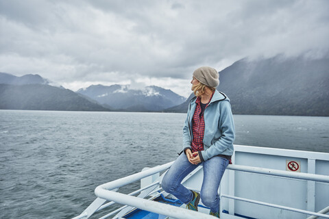 Chile, Hornopiren, woman sitting on rail of a ferry looking at fjord stock photo