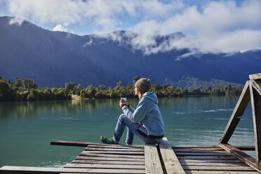 Chile, Chaiten, Lago Rosselot, Frau sitzt auf Steg und hält Becher - SSCF00214