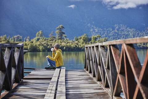 Chile, Chaiten, Lago Rosselot, woman sitting on jetty drinking from mug stock photo
