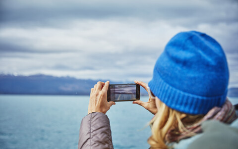 Chile, Puerto Rio Tranquilo, Frau macht Handyfoto von See und Berglandschaft, lizenzfreies Stockfoto