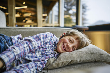 Happy boy lying on couch with earphones - SSCF00256