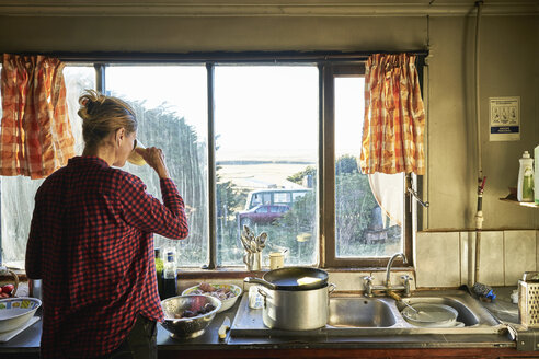 Frau steht in der Küche und bereitet eine Mahlzeit vor und trinkt aus einer Tasse - SSCF00264