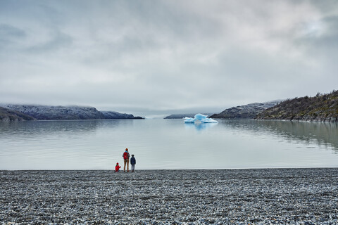 Chile, Torres del Paine Nationalpark, Lago Grey, Frau mit zwei Söhnen steht am Ufer und schaut auf einen Eisberg, lizenzfreies Stockfoto