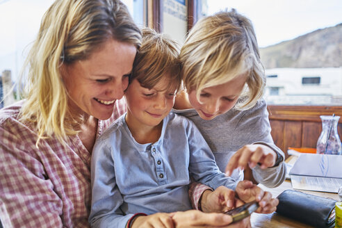 Glückliche Mutter mit zwei Söhnen sitzt am Tisch in einem Café und spielt mit dem Handy - SSCF00318