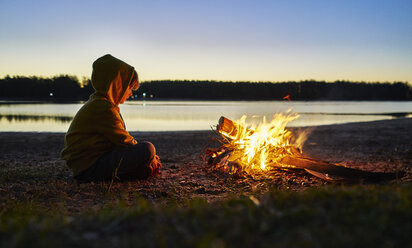 Argentinien, Patagonien, Concordia, Junge sitzt am Lagerfeuer an einem See - SSCF00340