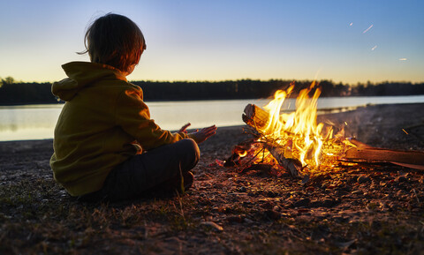 Argentinien, Patagonien, Concordia, Junge sitzt am Lagerfeuer an einem See, lizenzfreies Stockfoto