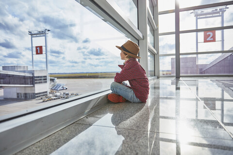 Boy sitting behind windowpane at the airport looking at airfield stock photo