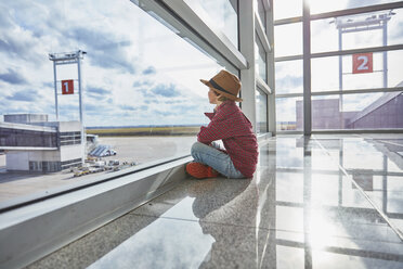 Boy sitting behind windowpane at the airport looking at airfield - SSCF00342