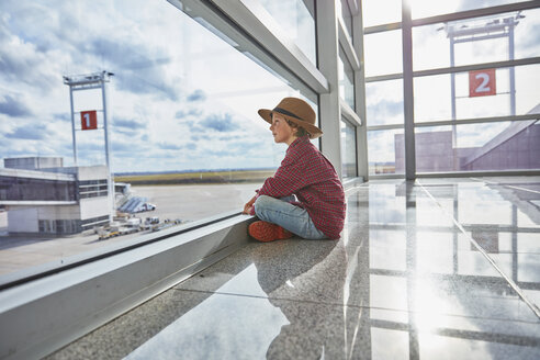 Junge sitzt hinter einer Fensterscheibe auf dem Flughafen und schaut auf das Flugfeld - SSCF00343