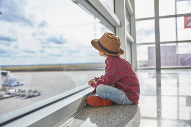 Boy sitting behind windowpane at the airport looking at airfield - SSCF00344