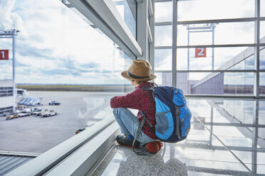 Boy sitting behind windowpane at the airport looking at airfield - SSCF00347