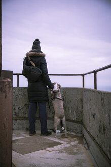Dänemark, Nordjütland, Rubjerg Knude Leuchtturm, Rückenansicht einer Frau mit Hund, die die Aussicht zur blauen Stunde betrachtet - REAF00486