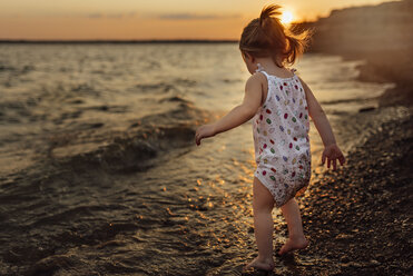 Baby-Mädchen in voller Länge am Ufer stehend bei Sonnenuntergang - CAVF59213