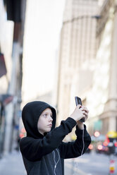 Junge fotografiert mit Smartphone in der Stadt stehend - CAVF59222