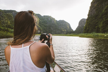 Rückansicht einer Frau beim Fotografieren während einer Bootsfahrt auf einem Fluss - CAVF59228