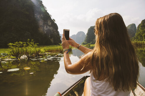 Rear view of woman photographing with mobile phone while traveling in boat on river - CAVF59231