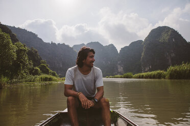 Man looking away while sitting in boat on river against sky - CAVF59232