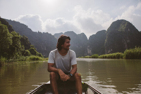 Man looking away while sitting in boat on river against sky - CAVF59232