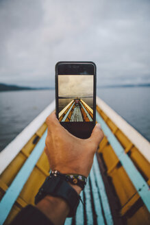 Abgeschnittene Hand, die ein Boot durch ein Smartphone gegen den Himmel fotografiert - CAVF59240
