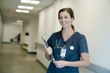 Portrait of cheerful female doctor holding laptop computer while standing in hospital lobby - CAVF59280