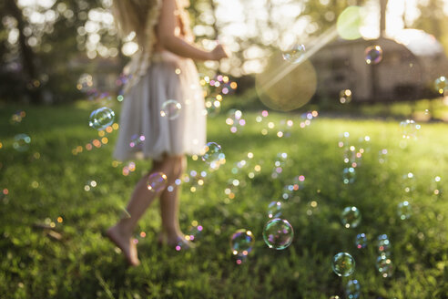 Low section of girl playing with bubbles on grassy field at park - CAVF59301