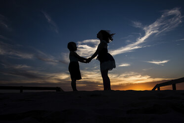 Silhouette Schwestern halten Hände, während sie auf einem Feld gegen den Himmel bei Sonnenuntergang stehen - CAVF59302