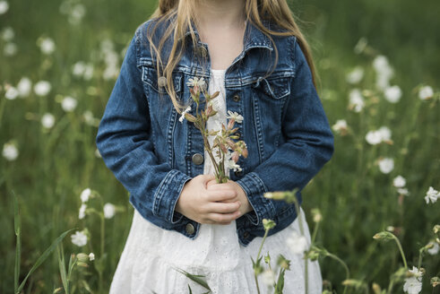 Mittelteil eines Mädchens, das Blumen hält, während es inmitten von Pflanzen auf einem Feld steht - CAVF59306