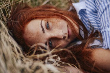 Close-up portrait of teenage girl with red head lying on grassy field - CAVF59335