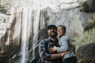 Porträt von fröhlichem Vater und Sohn vor einem Wasserfall im Yosemite-Nationalpark - CAVF59352