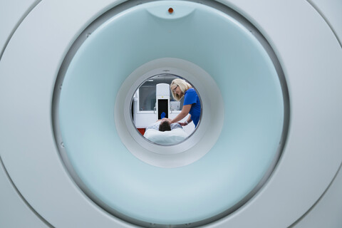 Krankenschwester bei der Vorbereitung eines Patienten auf eine MRT-Untersuchung im Krankenhaus, gesehen durch den Scanner, lizenzfreies Stockfoto