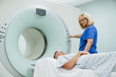Krankenschwester betrachtet den auf dem MRT-Scanner liegenden Patienten, während sie im Untersuchungsraum die Starttaste drückt - CAVF59376