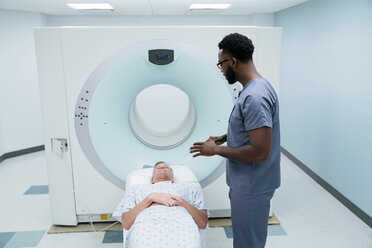 Seitenansicht eines Krankenpflegers im Gespräch mit einem Patienten, der für eine MRT-Untersuchung im Untersuchungsraum liegt - CAVF59380