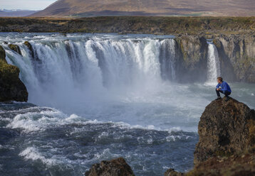 High angle view of hiker looking at waterfall while sitting on rock formations - CAVF59382