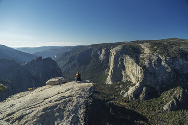 Frau sitzt auf einer Klippe im Yosemite National Park vor blauem Himmel - CAVF59383