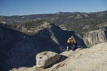 Seitenansicht einer Frau, die auf einer Klippe im Yosemite National Park sitzt, vor blauem Himmel - CAVF59385