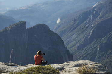 Mann beim Fotografieren auf einer Klippe im Yosemite National Park sitzend - CAVF59386