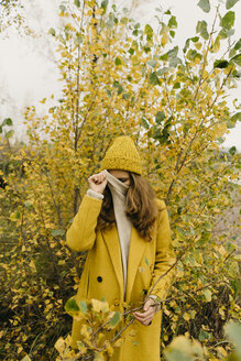 Woman covering face while standing against plants during autumn - CAVF59393