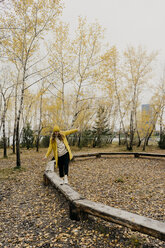 Verspielte Frau, die im Herbst auf Holzbänken im Park spazieren geht - CAVF59395