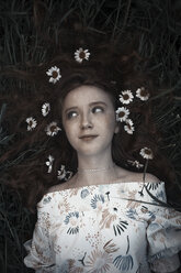 High angle view of teenage girl with flowers on hair lying on field - CAVF59407