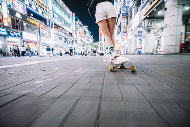 Niedriger Ausschnitt einer Skateboard fahrenden Frau auf einem Fußweg in einer beleuchteten Stadt bei Nacht - CAVF59447