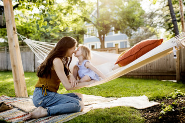 Daughter kissing mother while sitting in hammock at yard - CAVF59476