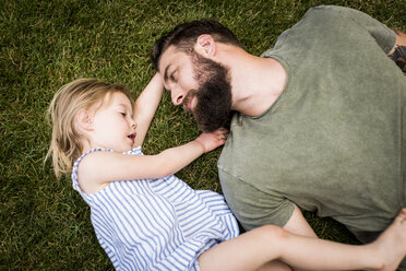 High angle view of father with daughter lying on grassy field at yard - CAVF59482