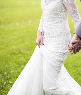 Ausgeschnittenes Bild eines frisch verheirateten Paares, das sich beim Gehen auf einer Wiese an den Händen hält - CAVF59488
