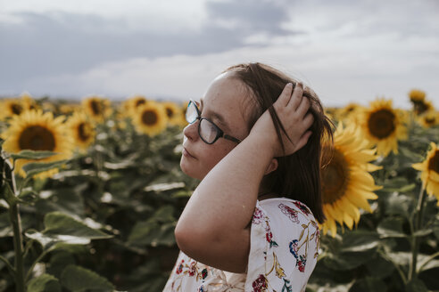 Nahaufnahme eines Mädchens mit Hand im Haar in einem Sonnenblumenfeld vor dem Himmel - CAVF59493