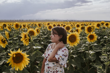 Girl looking away while standing in sunflower farm against sky - CAVF59494