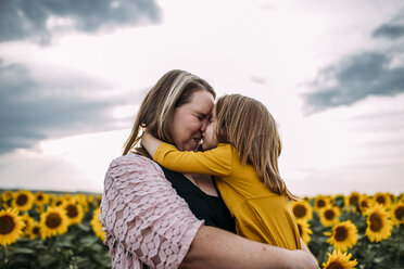 Mother and daughter embracing while standing in sunflower farm against sky - CAVF59497