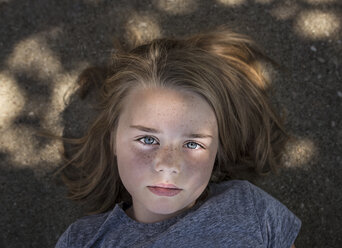 Overhead portrait of confident girl lying on road - CAVF59498